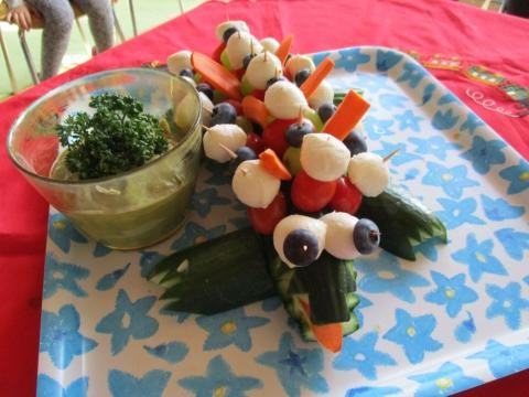 Aus Gruke, Kartotten, Tomaten und Mozarella ist ein Krokodil entstanden. Daneben steht ein Glas mit Avocado Dip